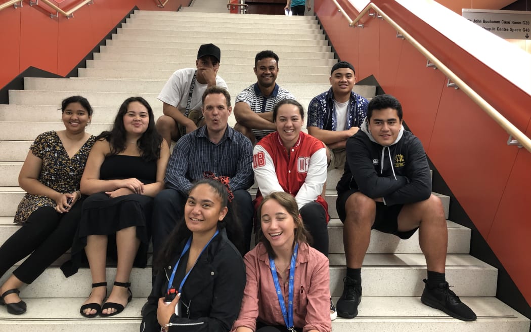 Dr Taniela Lolohea with high school students sitting on steps.