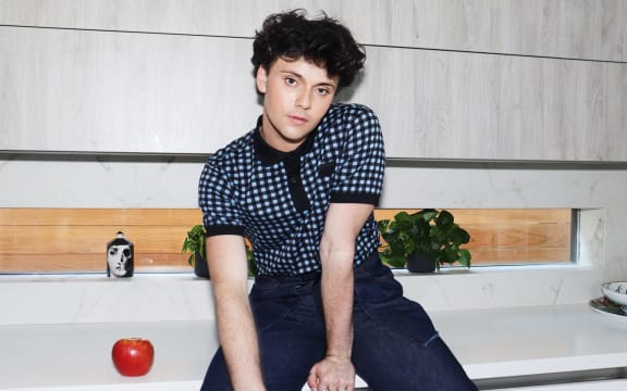 Musical artist Luca George sits on a kitchen benchtop alongside an apple