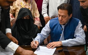 Pakistan's former Prime Minister, Imran Khan (R) along with his wife Bushra Bibi (C) signs surety bonds for bail in various cases, at a registrar's office in the High court, in Lahore on July 17, 2023. (Photo by Arif ALI / AFP)