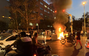 Demonstrators gather around a burning barricade during a protest for Mahsa Amini, a woman who died after being arrested by the Islamic republic's "morality police", in Tehran on September 19, 2022. - Fresh protests broke out on September 19 in Iran over the death of a young woman who had been arrested by the "morality police" that enforces a strict dress code, local media reported. Public anger has grown since authorities on Friday announced the death of Mahsa Amini, 22, in a hospital after three days in a coma, following her arrest by Tehran's morality police during a visit to the capital on September 13. (Photo by AFP)