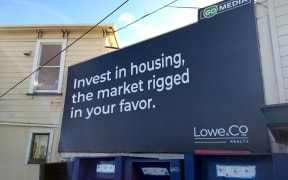 An image of a billboard proclaiming "Invest in housing, the market rigged in your favour."