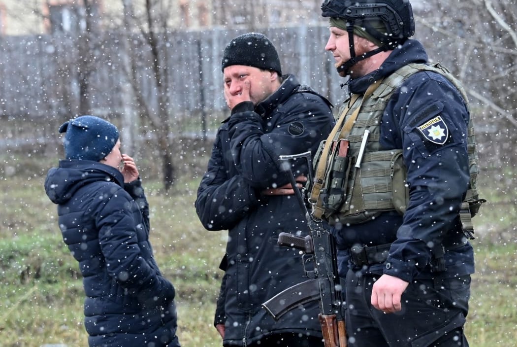 People gather close to a mass grave in the city of Bucha, just northwest of the Ukrainian capital Kyiv on 3 April, 2022.