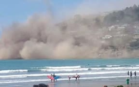 People on the beach at Sumner as a cliff collapses.