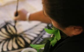Steady hands  in the final stages of Tongan ngatu making, adorning the ngatu with intricate Tongan symbols and designs.