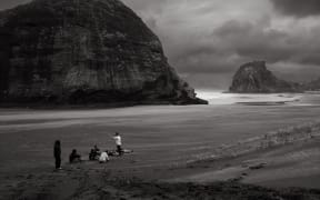 A group of people sit on a beach in a circle listening to a high performance coach.