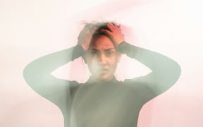 A woman in soft focus holds her hands to her head and frowns.