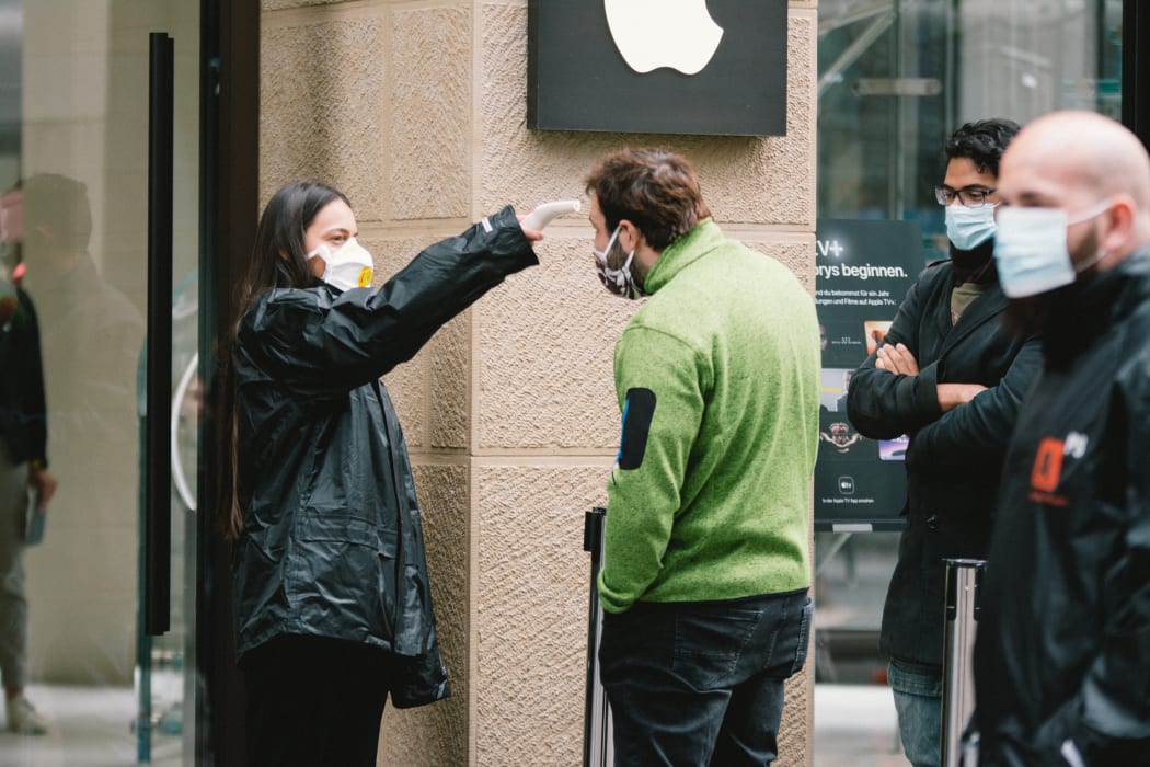 A staff member checks the body temperature of a customer before entering the Apple store in Cologne, Germany