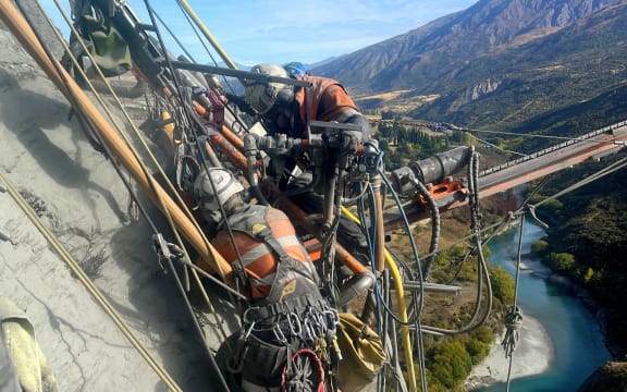 Workers and gear hanging off the side of a cliff.