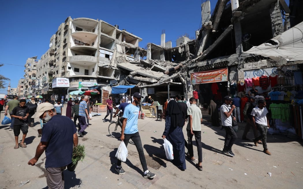 Palestinians walk past a destroyed building at a makeshift market in the Nuseirat refugee camp, located in the central Gaza Strip, on 15 October 2025, two days after a ceasefire came into effect.