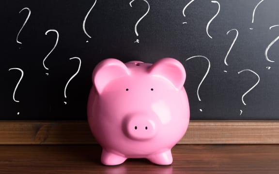 A file photo shows a piggy bank in front of a blackboard with question marks.