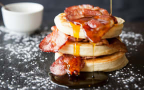 Female hand pouring maple syrup over breakfast bacon crumpet on slate