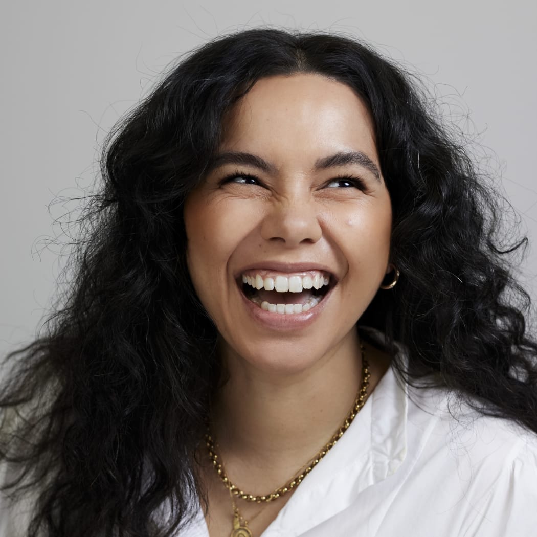 Courtney Dawson laughs. She is wearing a white shirt and a gold chain necklace.