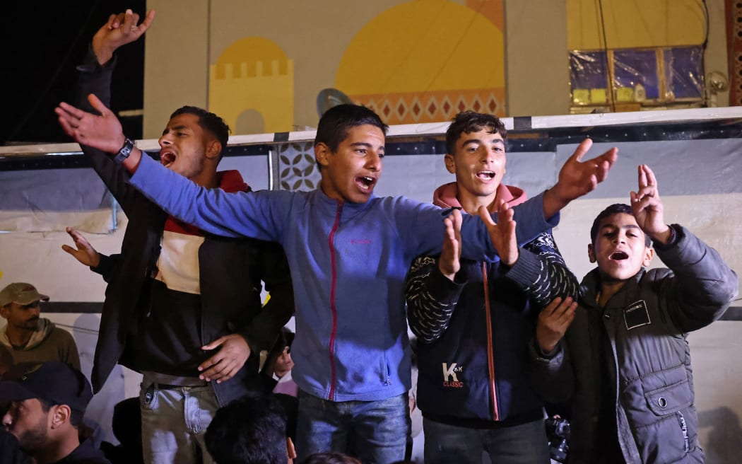 People celebrate while watching a television along a street in Khan Yunis in the southern Gaza Strip on January 15, 2025, amid the ongoing war in the Palestinian territory between Israel and Hamas. Thousands of Gazans celebrated on January 15 as news spread that a ceasefire and hostage release deal had been reached between Israel and Hamas, aimed at ending more than 15 months of war in the Palestinian territory. (Photo by BASHAR TALEB / AFP)