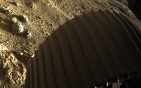 This NASA photo released on February 19, 2021, shows an image from NASAs Perseverance rover of the surface of Mars and one of the rover's wheels after landing on February 18, 2021.