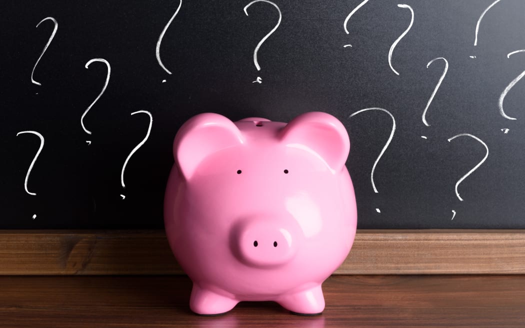 A file photo shows a piggy bank in front of a blackboard with question marks.
