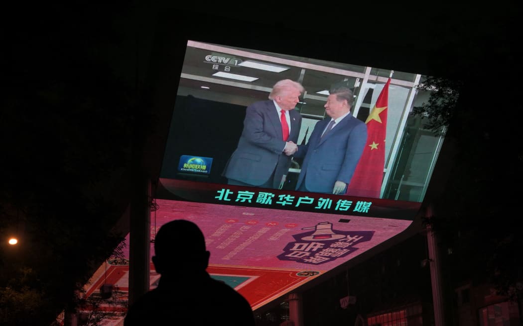 A screen shows news coverage of the meeting between US President Donald Trump and China's President Xi Jinping in South Korea, outside a shopping mall in Beijing on October 30, 2025. Donald Trump and Xi Jinping agreed on October 30 to calm the trade war between China and the United States that has roiled global markets, with Washington cutting some tariffs and Beijing committing to keep supplies of critical rare earths flowing. (Photo by Adek BERRY / AFP)