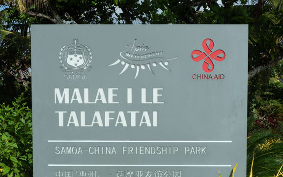 A large grey welcome sign with white text, surrounded by gardens. It reads: "MALAE I LE TALAFATAI - SAMOA CHINA FRIENDSHIP PARK".