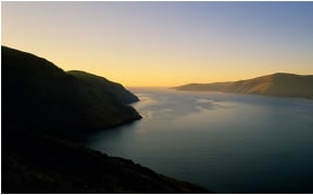 Sunrise at the entrance to Lyttelton harbour in Canterbury in the South Island of New Zealand. Golden glow on the horizon of Lyttelton Heads.