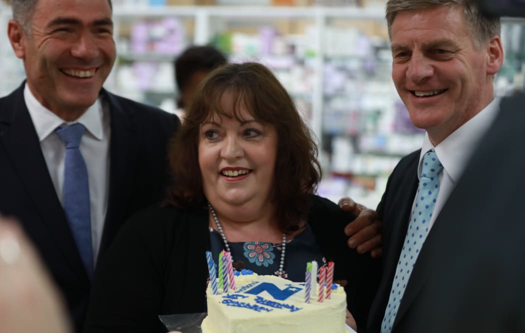 National Party leader Bill English, celebrates the birthday of a pharmacy employee, centre, during National's bus tour on Thursday. National MP Nathan Guy at left.
