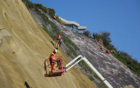Contractors scale the near vertical slopes of the cliffs above Rocks Road.