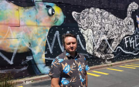 Capital and Coast Health nurse and therapist Dion Howard in front of the tagged Five Giant Rabbits mural.