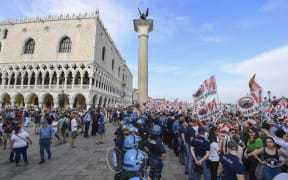 Police officers face people holding flags as they arrive close to San Marco square during a demonstration called by the No Great Ships movement against big cruise ships sailing into the Venice.
