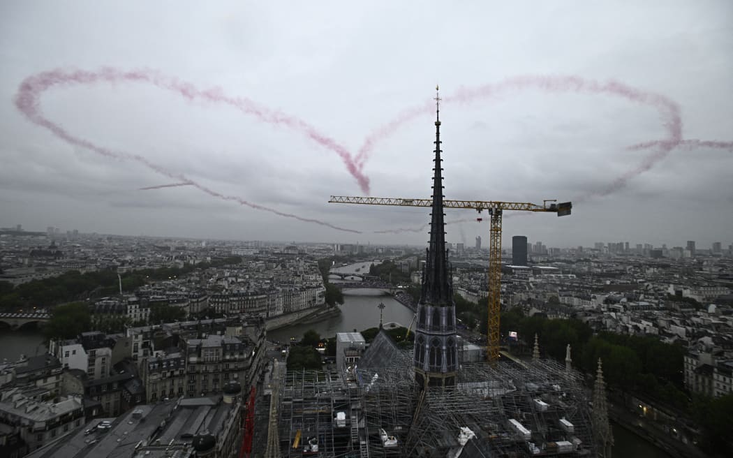 A heart made with red smoke by 4 planes floats in the air near Notre-Dame Cathedral during the opening ceremony of the Paris 2024 Olympic Games in Paris on July 26, 2024. (Photo by JULIEN DE ROSA / POOL / AFP)