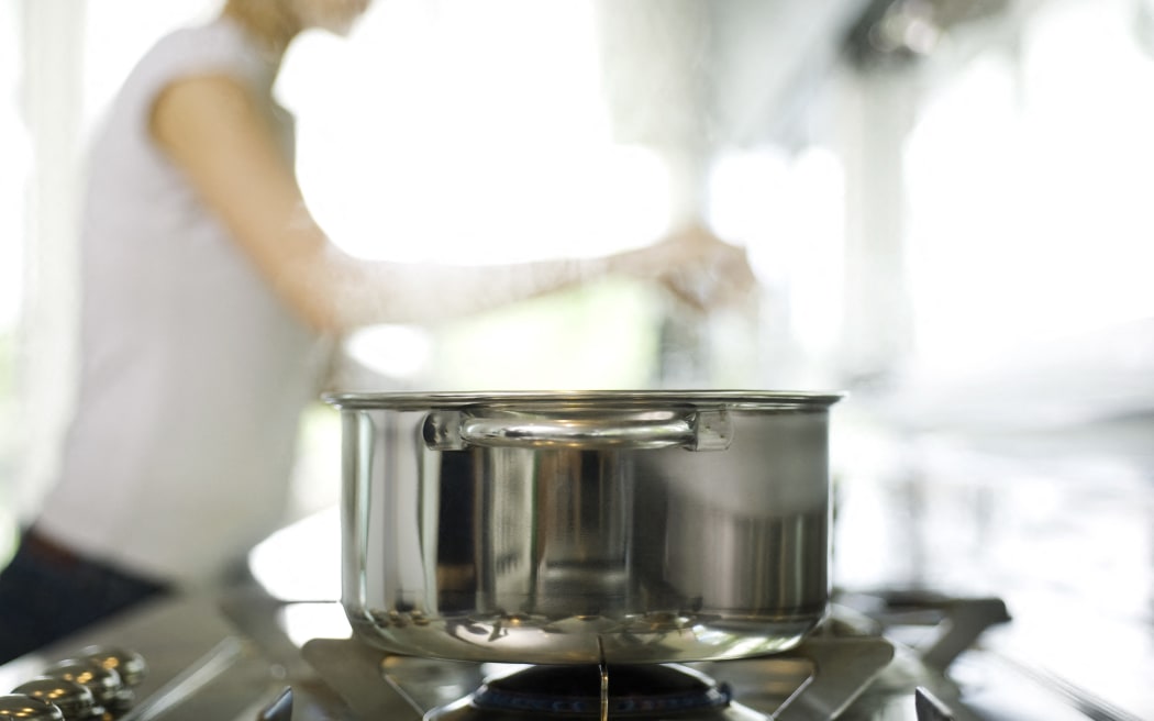 Pot cooking on stove, woman in background (Photo by Laurence Mouton / AltoPress / PhotoAlto via AFP)