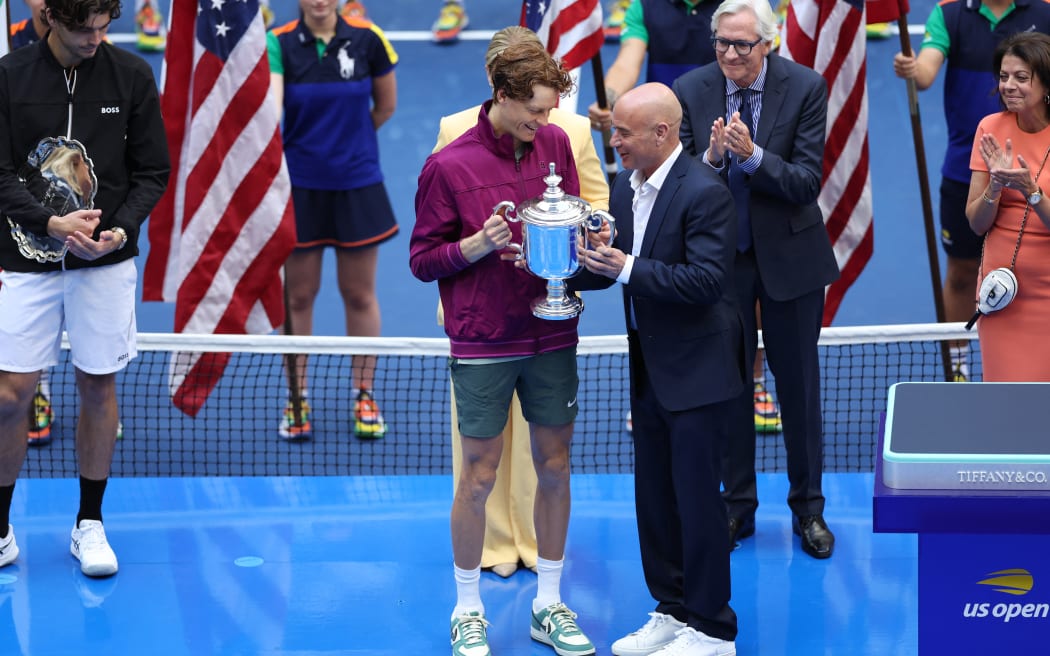 Italy's Jannik Sinner (C) receives the trophy after winning his men's final match against USA's Taylor Fritz (L) on day fourteen of the US Open tennis tournament at the USTA Billie Jean King National Tennis Center in New York City, on September 8, 2024. (Photo by CHARLY TRIBALLEAU / AFP)