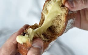 Two hands pull apart a golden doughnut that is oozing pale yellow vanilla custard.