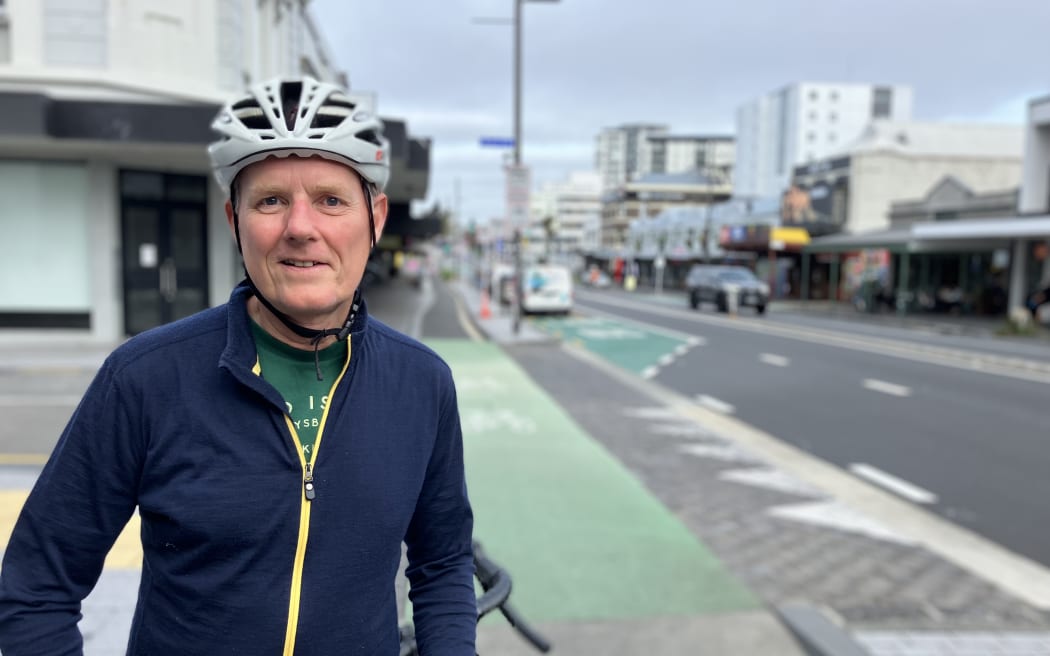A man, wearing a helmet, standing next to his bike on the Karangahape Road cycleway.