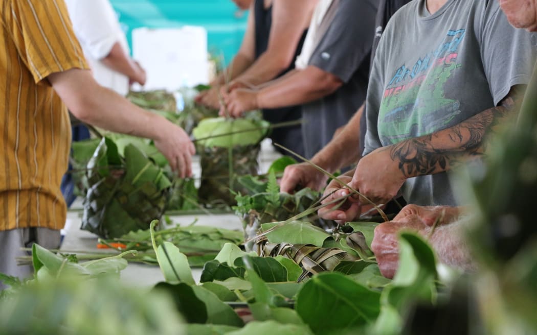 Whānau prepare traditional hāngi, placing kai in rourou baskets that were weaved by volunteers.