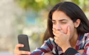 A photo of a worried teenager girl looking at her smart phone in a park with an unfocused background