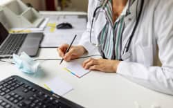 Close-up of a doctor preparing prescription while consulting a patient over video conference. Female doctor making notes while talking with patient on video call.