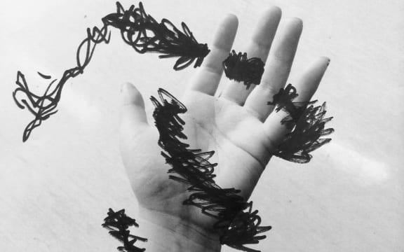 A hand is obscured by black scribbles, to illustrate struggles with mental health