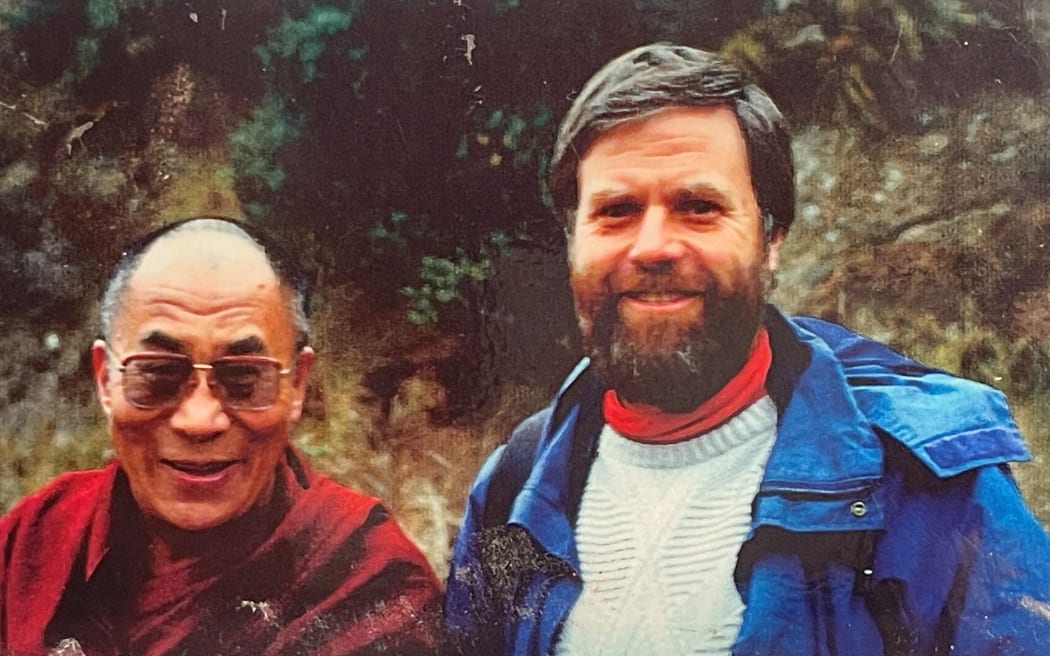 The Dalai Lama and Dean pose for a photo. They both smile.