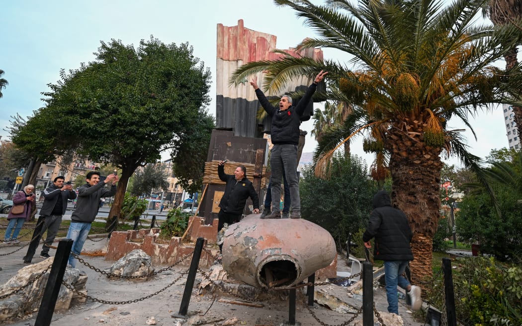 People stand atop a toppled statue of Syria’s late president Hafez al-Assad in Damascus on December 8, 2024. - Islamist-led rebels declared that they have taken Damascus in a lightning offensive on on December 8, sending President Bashar al-Assad fleeing and ending five decades of Baath rule in Syria. (Photo by LOUAI BESHARA / AFP)