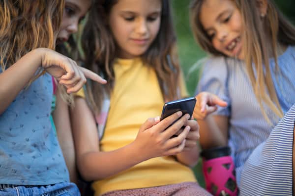 Three young girls talking and pointing at one of their phone screens.