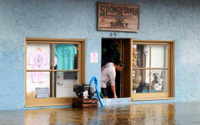 A store owner in Tarpon Springs, Florida, uses a pump to try to keep water out of his store after Hurricane Idalia passed offshore on 30 August 2023.