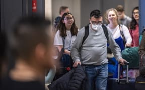 A passenger arriving from Brussels wearing a mask to protect himself from the new coronavirus looks for his relatives in the International arrivals zone at Dulles airport outside Washington,DC.