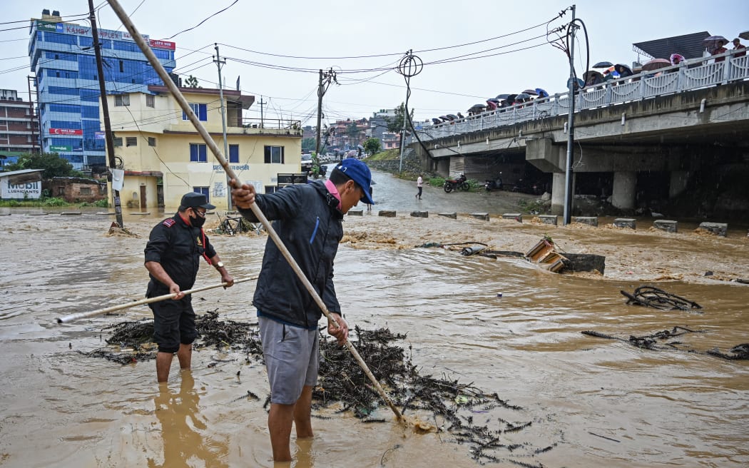 Residents clean a flooded street after the Balkhu river overflowed during monsoon rains in Kathmandu on September 28, 2024. Floods and landslides caused by heavy downpours in Nepal killed at least 10 people across the Himalayan country, with rescue teams searching for 18 missing, a disaster official said on September 28. (Photo by PRAKASH MATHEMA / AFP)