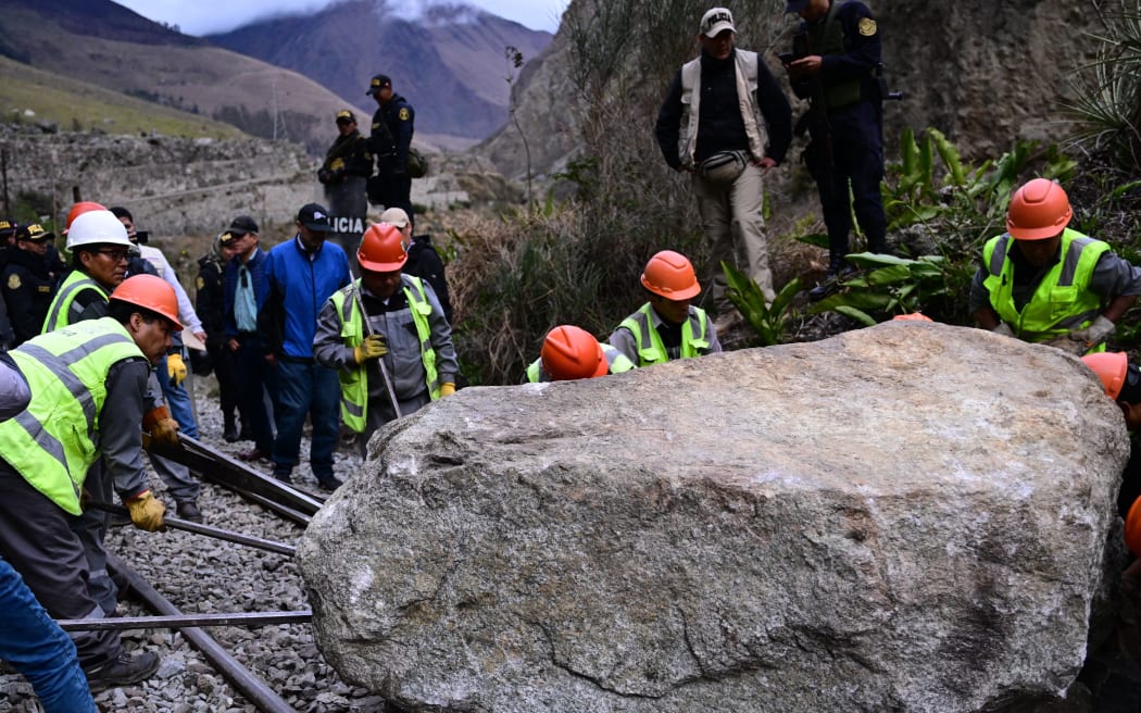 Workers attempt to remove a rock placed by rioters on the railway track to block the train's passage to and from the Inca citadel of Machu Picchu in Ollantaytambo, Peru, on December 17, 2022. - Around 5,000 tourists have been left stranded in Cusco, the gateway city to Peru's top attraction Machu Picchu, by deadly protests against the ousting of president Pedro Castillo, a local mayor said on Friday. Rail service to Machu Picchu has been suspended since Tuesday. (Photo by MARTIN BERNETTI / AFP)