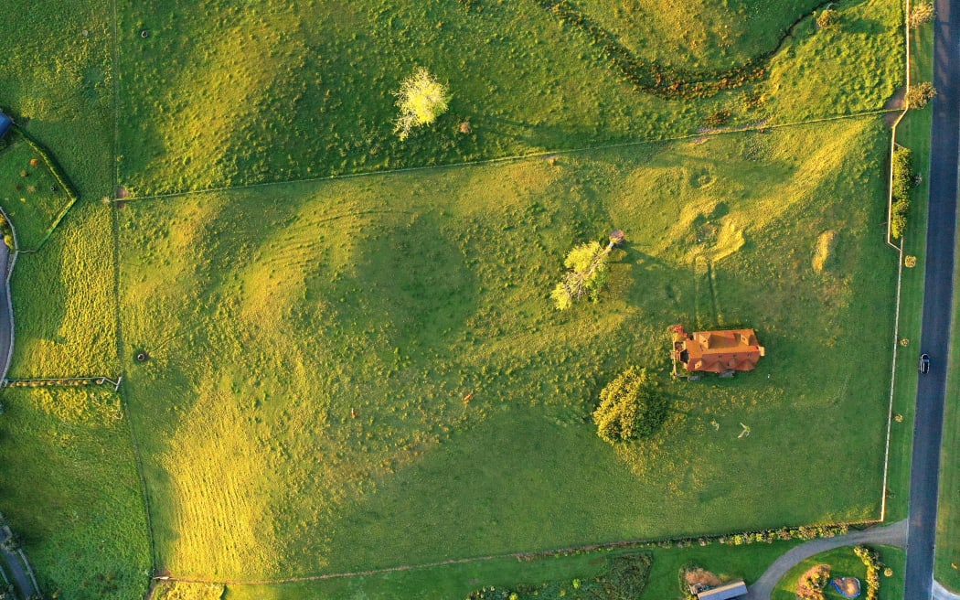 A birds eye view of the Kaipara Lake Rd house, surrounded by a lush green field.
