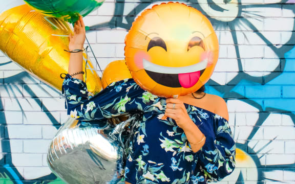 A person holding a smiley balloon in front of their face.