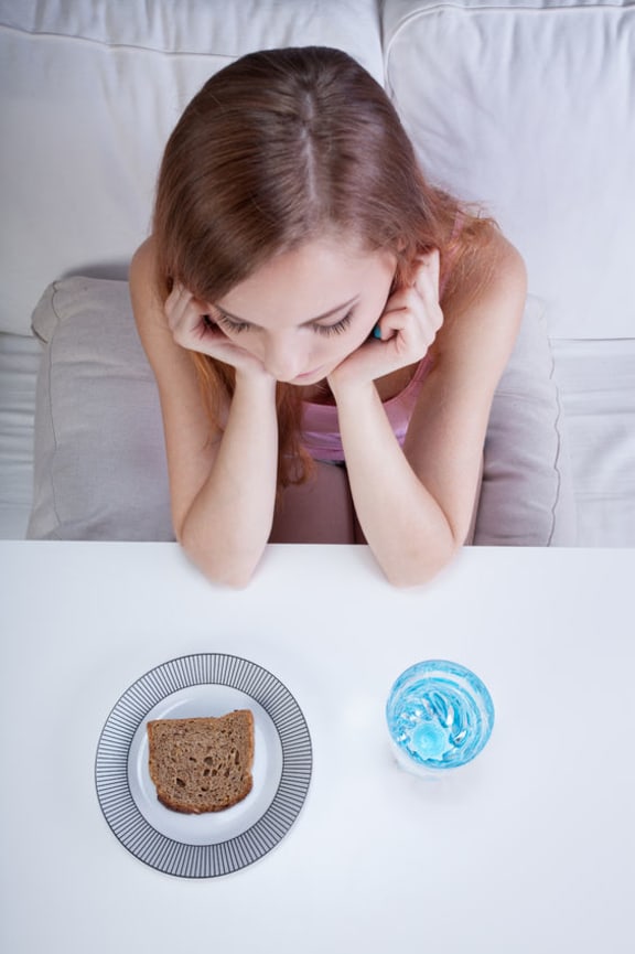 A photo of a girl looking at her dinner which is just bread and water