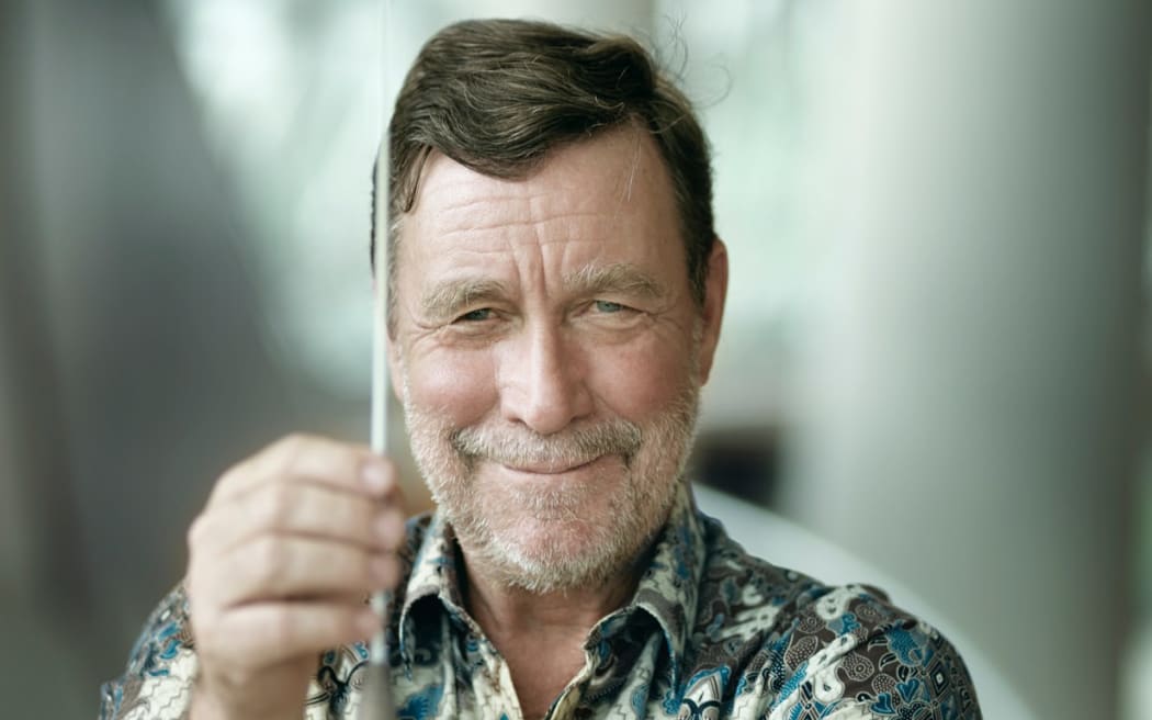 Headshot of Finnish conductor Okko Kamu, smiling and holding his baton in front of his face