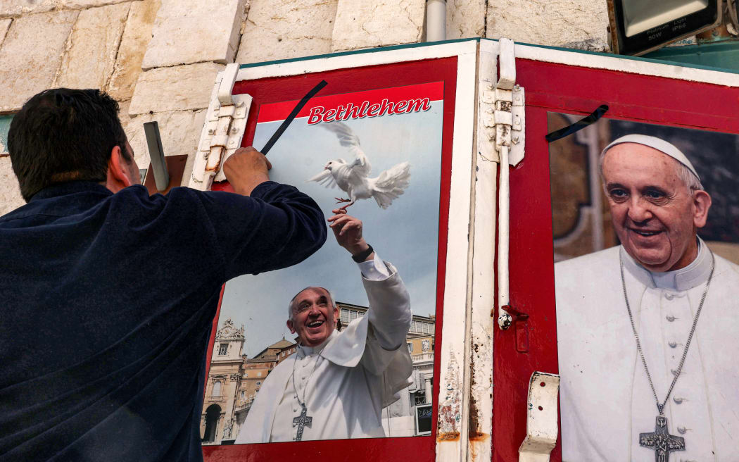 A man pastes a picture of the late Pope Francis outside a shop in the biblical city of Bethlehem in the occupied West Bank on April 21, 2025. Pope Francis died on April 21, 2025 aged 88, a day after making a much hoped-for appearance at Saint Peter's Square on Easter Sunday, the Vatican said in a statement. (Photo by HAZEM BADER / AFP)