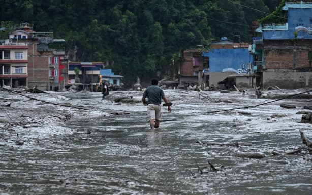 A resident walks along a street covered in mud following flash floods and a landslide disaster in Devighat, in Nepal's Nuwakot district on August 26, 2026. A massive flood and landslide disaster on the Nepal-Tibet border killed at least 103 people on August 26, 2026 and left several hundred missing, many of them foreign tourists. Aid workers said entire settlements had been "wiped out". Some 403 tourists -- 341 of them foreigners -- were unaccounted for several hours after the disaster struck, according to the tourism ministry. (Photo by PRAKASH MATHEMA / AFP)