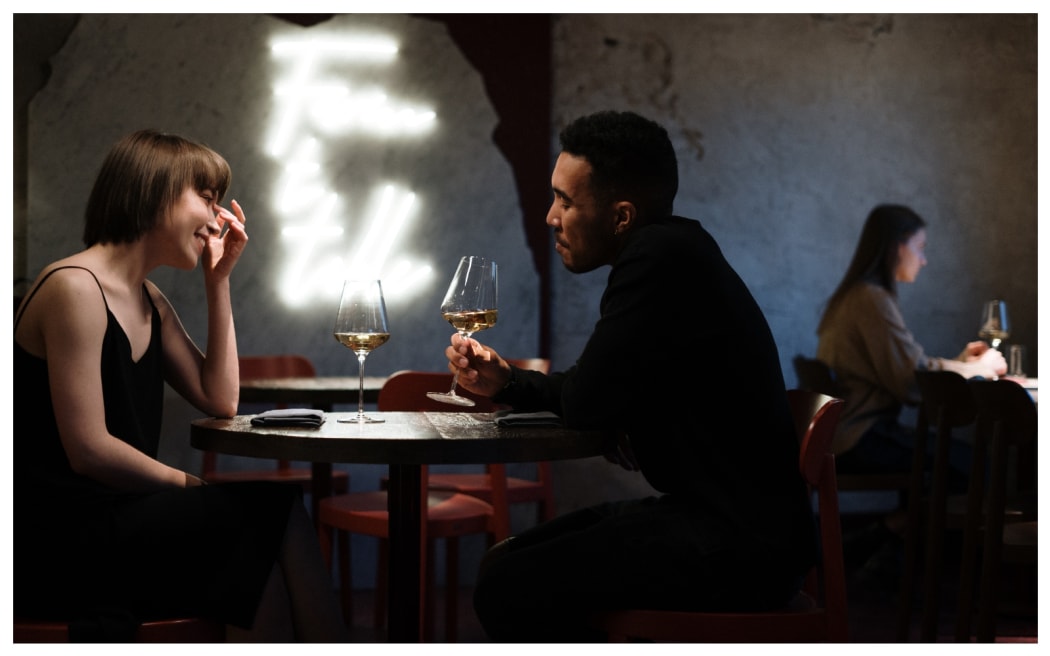A young woman sits opposite a man on a date. Each have a glass of wine.