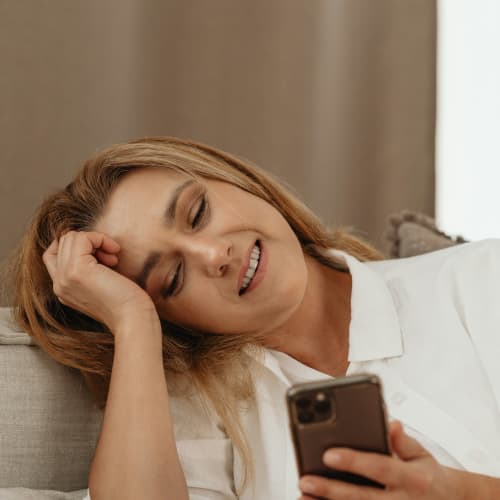 A blonde woman looks wistfully and happily at her mobile phone.